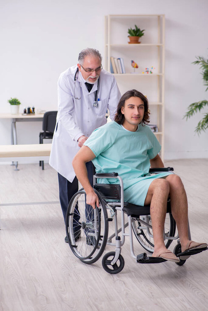 Junger männlicher Patient im Rollstuhl und erfahrener Arzt Traumatologe - Foto, Bild