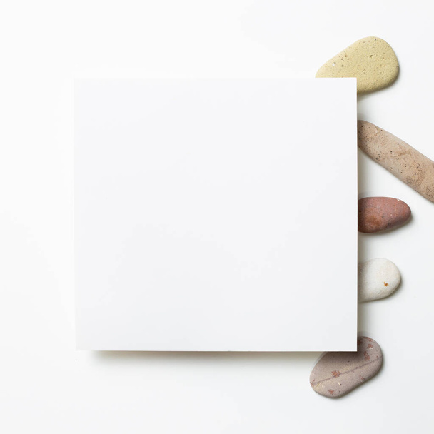Almohadilla blanca, papel vacío con piedras de guijarro sobre fondo blanco. plano, vista superior, espacio para copiar - Foto, Imagen