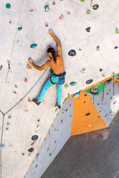 Een man beklimt een klimwand, een klimmer traint op kunstmatig terrein, rotsklimmen in de stad, een sterke man, sport in de stad, veiligheid in extreme sporten. - Foto, afbeelding