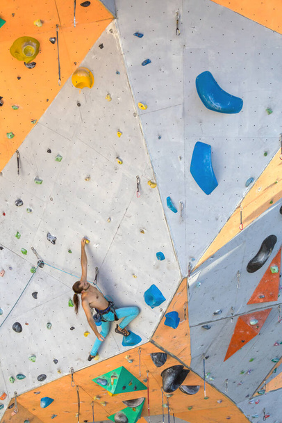 Un hombre trepa un muro de escalada, un escalador está entrenando en terreno artificial, escalada en roca en la ciudad, un hombre fuerte, deportes en la ciudad, seguridad en deportes extremos. - Foto, imagen
