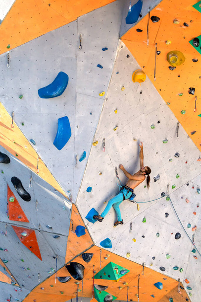 Mies kiipeää kiipeilyseinälle, kiipeilijä harjoittelee keinotekoisessa maastossa, kalliokiipeilyä kaupungissa, vahva mies, urheilu kaupungissa, äärimmäisten urheilulajien turvallisuus.. - Valokuva, kuva