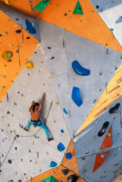 Um homem sobe uma parede de escalada, um alpinista está treinando em terreno artificial, escalada na cidade, um homem forte, esportes na cidade, segurança em esportes radicais. - Foto, Imagem
