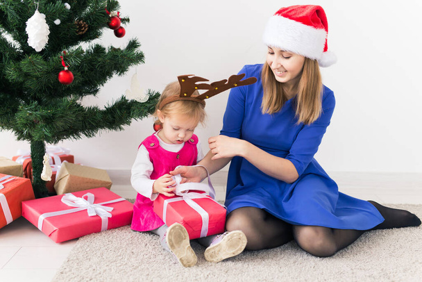 Smiling mother open Christmas presents with baby daughter in room at background. Winter season. Motherhood. Merry Christmas. New Year. - Photo, image