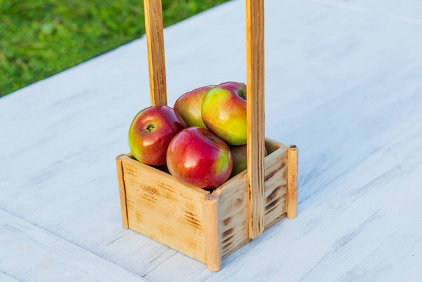 Luz del día. una cesta de madera con manzanas rojas. Estilo retro fondo de madera blanca. Envejecimiento artificial. - Foto, imagen