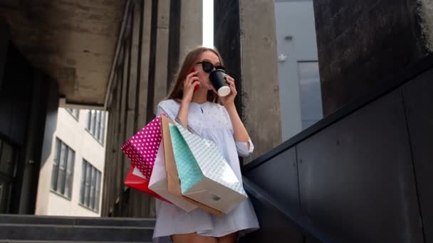 Meisje in de buurt van winkelcentrum met boodschappentassen en praten op mobiele telefoon over aankopen - Video