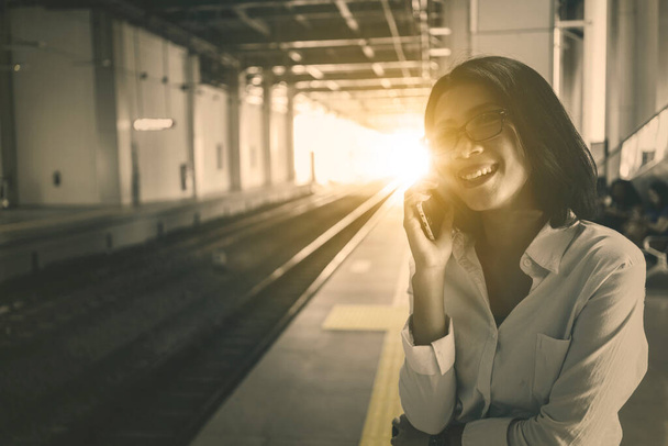 Young businesswoman makes a calling phone while standing in the train station with sunlight at dusk time - Photo, Image