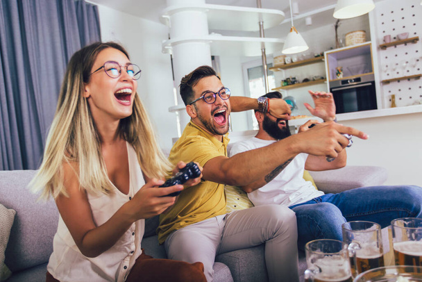 Grupo de amigos divirtiéndose sentados en el sofá en la sala de estar y jugando videojuegos en casa. - Foto, imagen