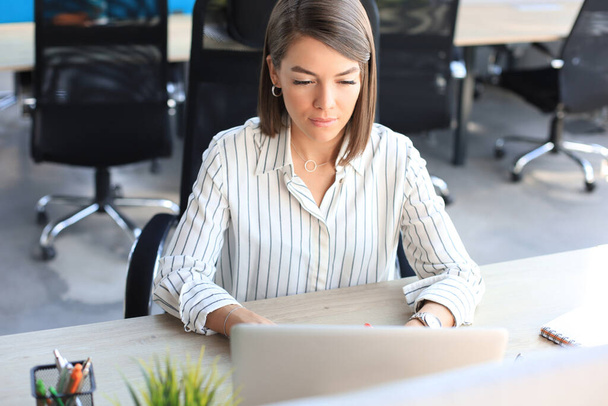 Beautiful business woman in smart casual wear working on laptop in the office. - Foto, afbeelding