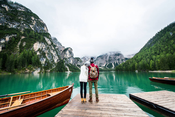 Beautiful couple of young adults visiting an alpine lake at Braies, Italy - Tourists with hiking outfit having fun on vacation during autumn foliage - Concepts about travel, lifestyle and wanderlust - Foto, imagen