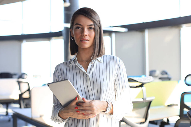 Portrait of young businesswoman holding touch pad while standing in modern office space interior - Photo, image