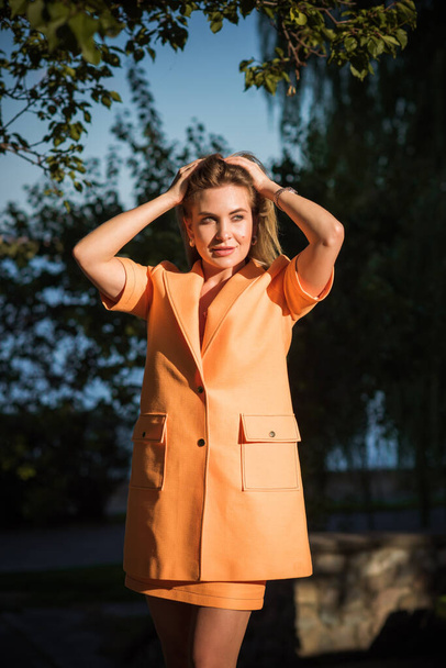 Frau in orangefarbenem Mantel auf der Straße, Frau im Outfit. Schicker Stil für Damen, Herbstfarben und Mode  - Foto, Bild