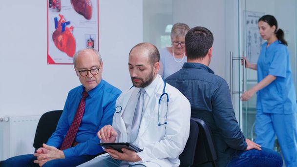 Arzt diskutiert Diagnose mit altem Mann im Krankenhaus-Wartebereich - Foto, Bild