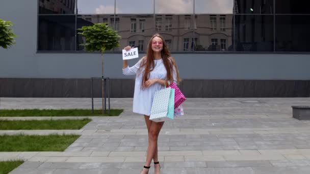 Junges stylisches Mädchen zeigt Sale Word Inschrift Text, lächelt, sieht zufrieden mit niedrigen Preisen - Filmmaterial, Video