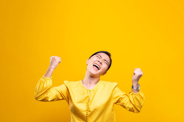 Glückliche Frau macht Siegergeste auf gelbem Hintergrund - Foto, Bild