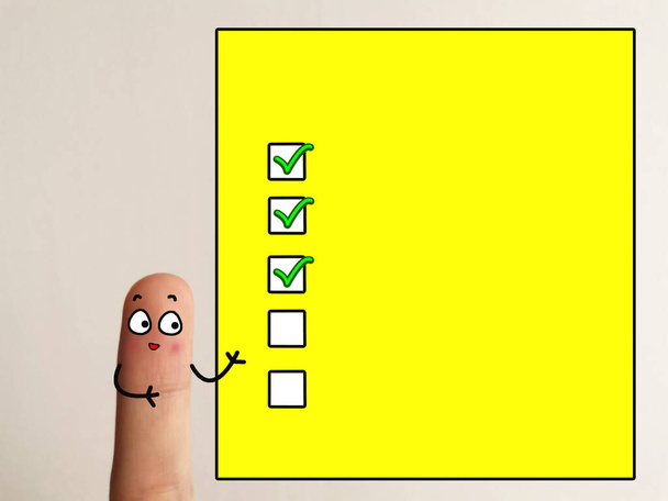 Ein Finger ist als eine Person dekoriert. Die Person steht neben einem gelben Bildschirm mit drei Häkchen darauf. - Foto, Bild