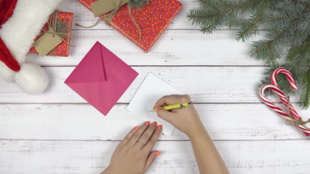 A fiatal lány levelet írt a Mikulásnak, és betette egy borítékba. Karácsonyi dekorációk és ajándékdoboz a fa íróasztalon, felülnézetből. A szilveszter koncepciója. - Felvétel, videó