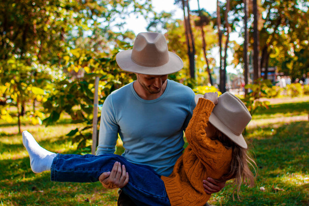 Χαριτωμένη μικρή κόρη σε ένα κίτρινο πουλόβερ παίζει με ένα νεαρό μπαμπά σε ένα πάρκο φθινόπωρο - Φωτογραφία, εικόνα