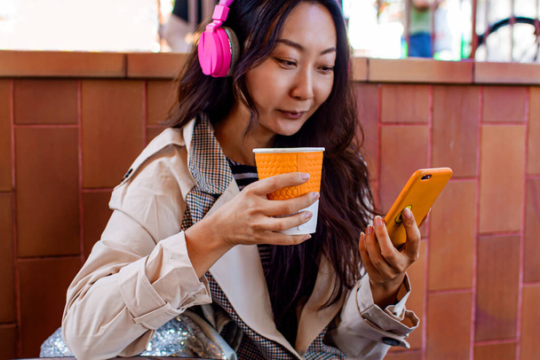 Een student met een koptelefoon en een smartphone drinkt koffie bij de muur. - Foto, afbeelding