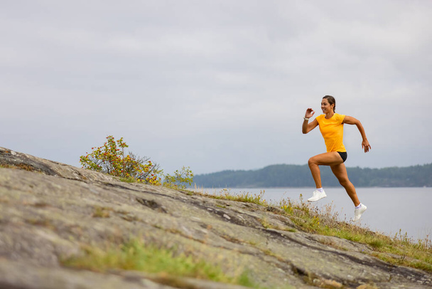 Vista lateral de la mujer fitness haciendo carreras de alta intensidad en la ladera de la montaña junto al mar - Foto, Imagen
