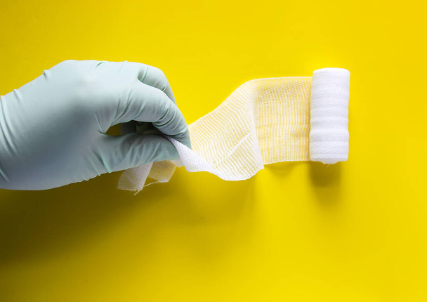 Hand in Latex-Handschuh, der die medizinische Binde auf leuchtend gelbem Hintergrund hält - Foto, Bild