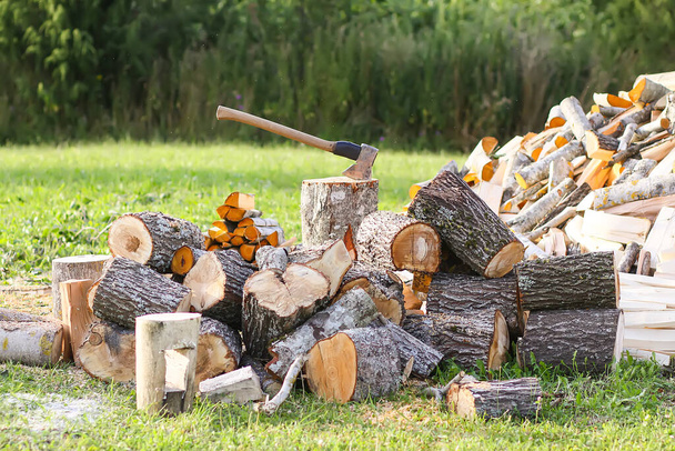 Bois de chauffage haché et hache en bois sur champ vert. Récolte du bois de chauffage pour la saison hivernale. - Photo, image
