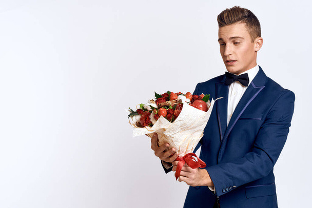 An elegant man in a classic suit with a bow tie holds a bouquet of flowers in his hand  - Photo, Image