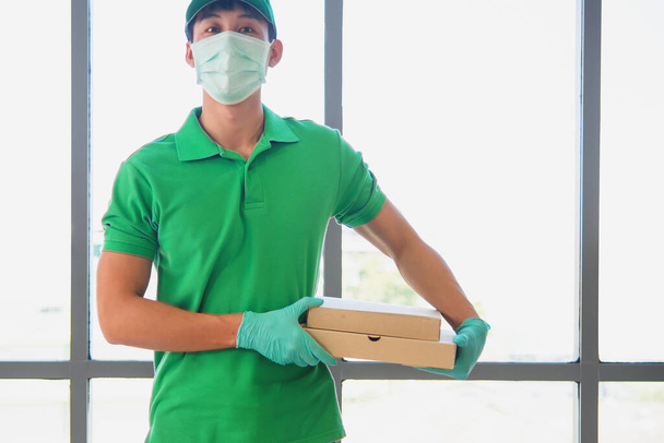 Groen uniform bezorger met chirurgisch masker en handschoen leveren pizza pakket - Foto, afbeelding