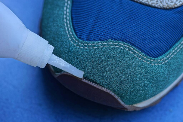 white tube in hand glue the sock of a suede and leather sneaker on a blue background - Photo, Image