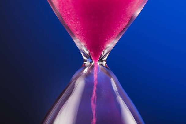 Яркий розовый песок с песочными часами на синем фоне - Фото, изображение