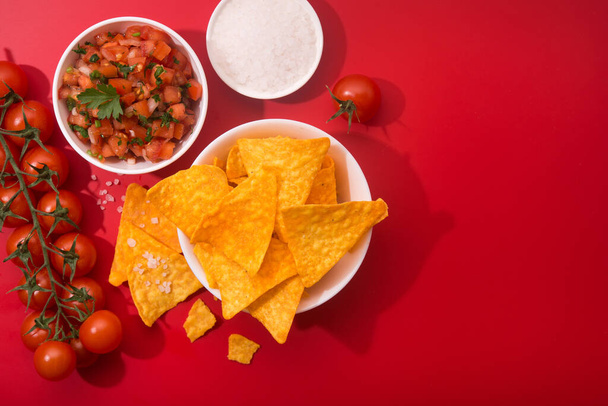 Хрустящие чипсы с сальсой и солью на красном фоне. Плоский лежал. Мексиканская кухня. - Фото, изображение