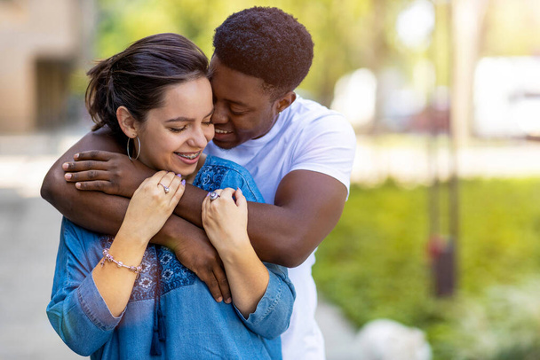 Affectionate multi-ethnic couple embracing outdoors - Фото, изображение