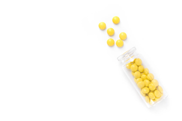 Gele pillen met glazen fles geïsoleerd op een witte achtergrond. bovenaanzicht - Foto, afbeelding