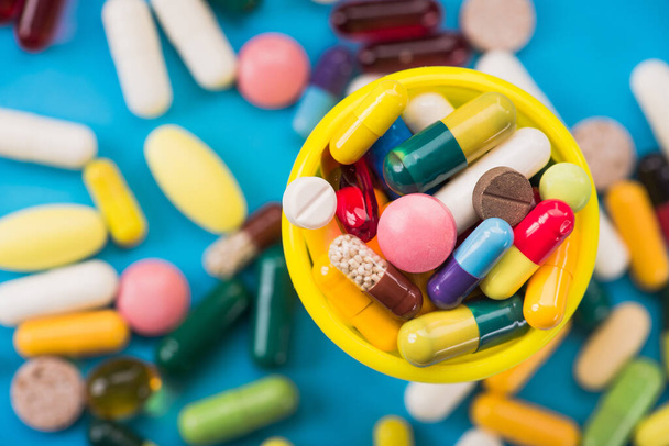 Muchas píldoras y cápsulas de color en un recipiente amarillo sobre un fondo azul. vista superior - Foto, Imagen