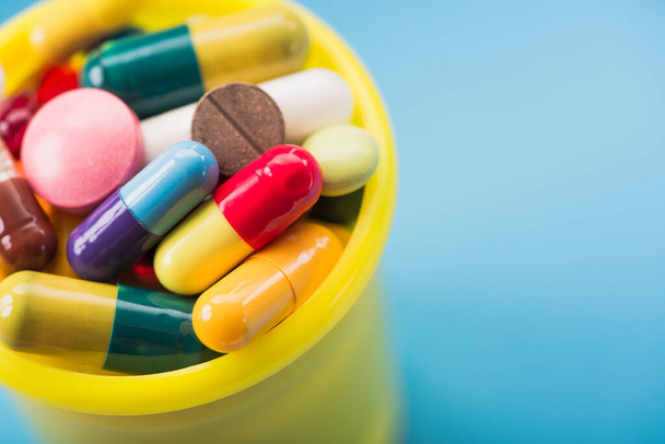 gros plan de nombreuses pilules et capsules de couleur dans un récipient jaune sur un fond bleu - Photo, image
