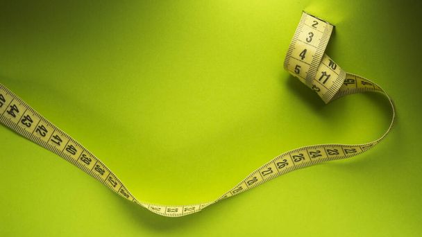 Closeup of yelllow measuring tape on a green background. Diet and weight loss. top or above view - Photo, Image