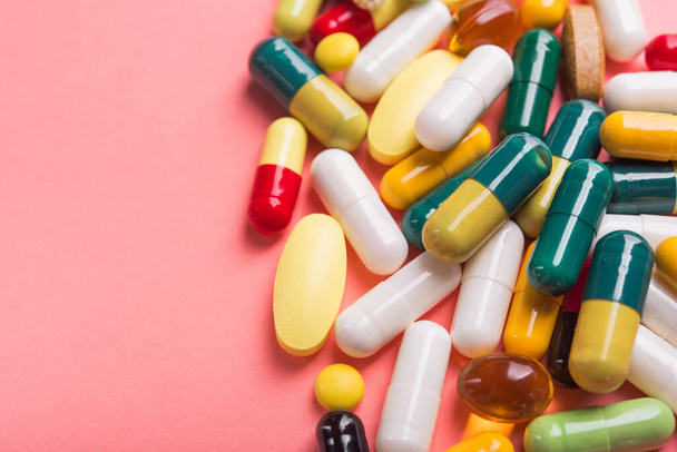 Stapel gekleurde pillen, capsule en tabletten op een pastelroze achtergrond. - Foto, afbeelding