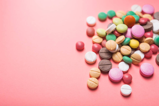 Un mucchio di pillole colorate, capsule e compresse su uno sfondo rosa pastello. vista dall'alto. posto per testo. - Foto, immagini