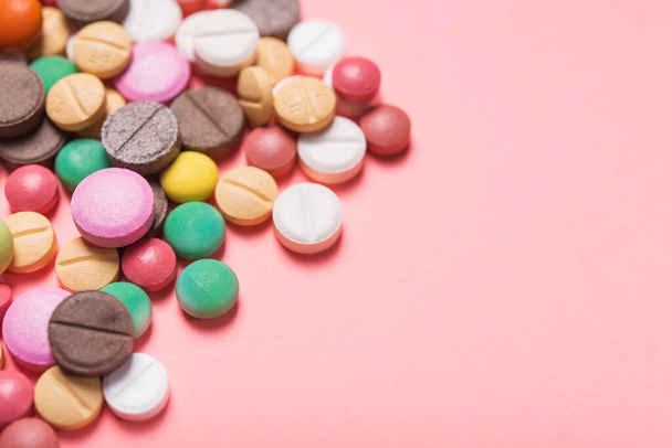 Montón de píldoras de colores, cápsulas y tabletas sobre un fondo rosa pastel. - Foto, imagen