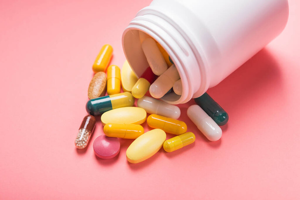 Flacon blanc de pilules et capsules de couleur médicale sur fond rose pastel - Photo, image