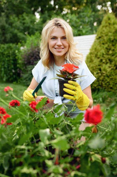 Happy young woman in gloves works with flower in the garden. Female gardener takes care of plants outdoor, gardening hobby, florist lifestyle - Foto, Imagem