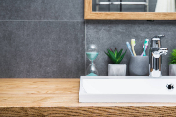 Φυσικό ξύλινο τραπέζι στο μπάνιο σκανδιναβικό στυλ με λευκό κεραμικό νεροχύτη και αξεσουάρ μπάνιου. Θέση για κείμενο. εκτός εστίασης - Φωτογραφία, εικόνα