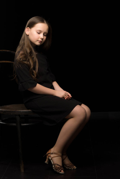 Portrait of a little girl sitting on an old Viennese chair, black background. - Foto, immagini