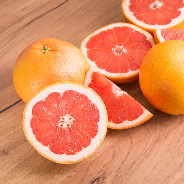 Detailní záběr krájených šťavnatých grapefruitových kousků na kuchyňském dřevěném stole. - Fotografie, Obrázek