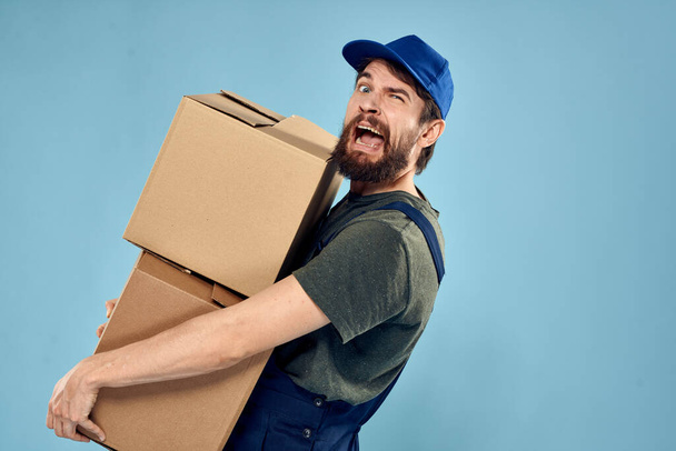 Homem em uniforme de trabalho com caixas em mãos serviço de entrega fundo azul - Foto, Imagem
