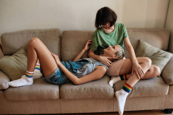 Homosexual couple of lesbian women looking at each other while relaxing together on the couch at home - Foto, Imagem