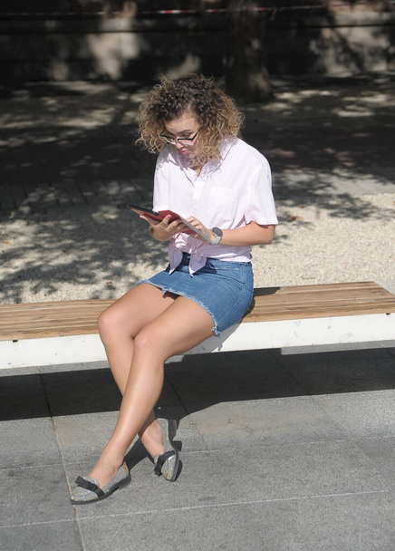  Кучеряве волосся жінка в масці працює на мобільному телефоні на відкритому повітрі
  - Фото, зображення