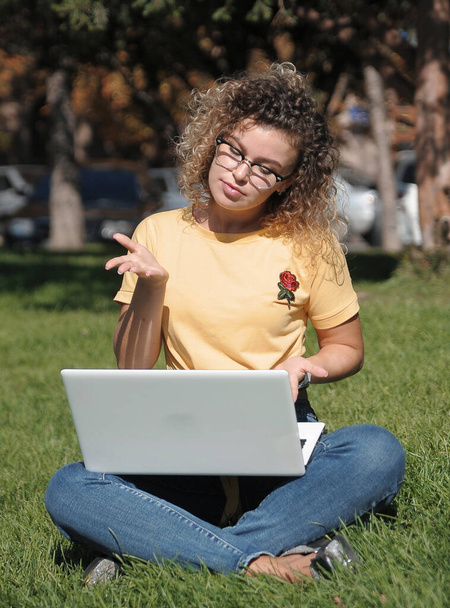 ラップトップを屋外に持つ若い女性。オンライン教育、遠隔教育の学生はラップトップで動作します. - 写真・画像