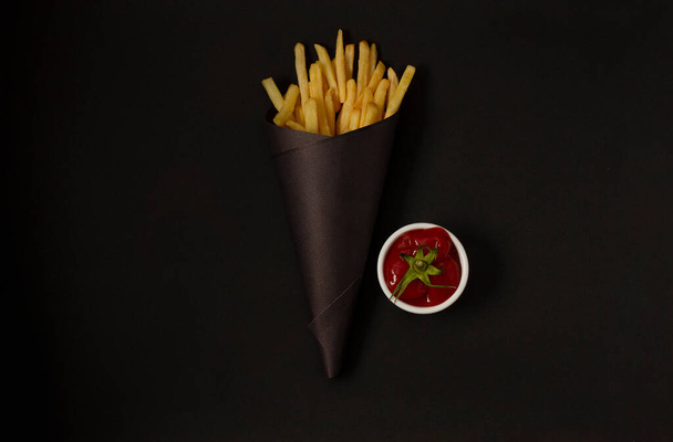 patatine fritte su fondo nero, con salsa di pomodoro in confezione nera, orizzontale - Foto, immagini