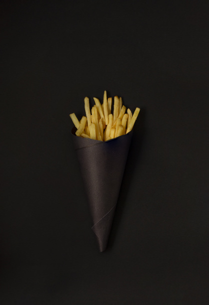 papas fritas sobre un fondo negro, en un paquete negro, vertical - Foto, imagen