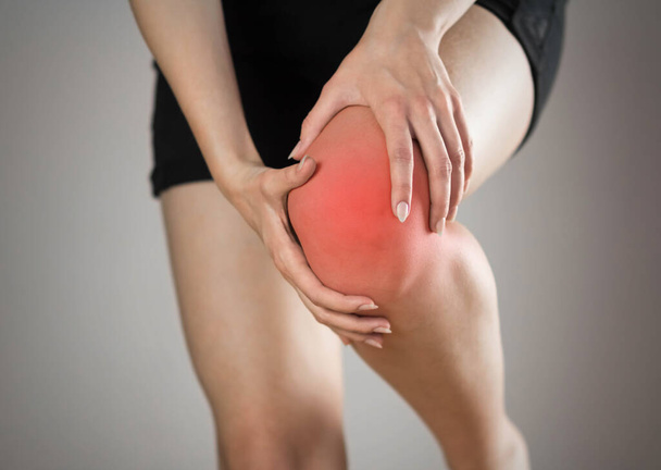 Pain in the knee of a woman. Highlighted in red. On a gray background. Close up. - Foto, Imagem